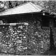 View of the women's restroom at Berkeley Park in Denver, Colorado. The stone building has a tiled roof and a painted sign that reads: "Ladies".