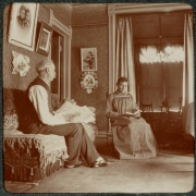A man and woman who read in their home in Denver, Colorado. Photographs and paintings hang on the walls. The man holds a newspaper titled "Brown Book".