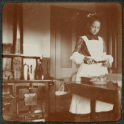 A maid who wears an apron prepares food in the kitchen of a house in Denver, Colorado. A stove and coffee pot are nearby.