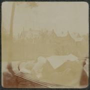 A man sleeps outdoors on a wooden bench in his backyard in Denver, Colorado. Houses are in the distance.