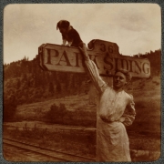 A woman poses with a puppy near a sign that reads: "36 Park Siding" on the Colorado and Southern Railway (C&S) route at Park Siding, (Jefferson County), Colorado. Railroad tracks are nearby.