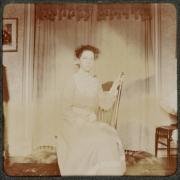A woman poses indoors on a rocking chair in a house in Denver, Colorado. She wears a long dress.