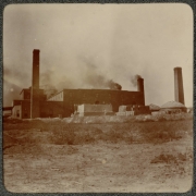 View of the Denver Engineering Works Company's buildings at 30th (Thirtieth) and Blake Streets in Denver, Colorado. Supplies are stacked outside near the smokestacks.