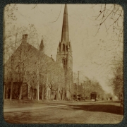View of church in Denver, Colorado. The building has a steeple and arched windows. A Denver Tramway Company trolley car and a horse-drawn buggy make their way by the church.