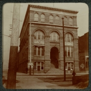 A man stands near the Denver Chamber of Commerce building at 14th (Fourteenth) and Lawrence Streets in Denver, Colorado. Signs read: "A. D. 1884", "Board of Trade", "1104", "1102 Bicycle Repairing", and "Printing".