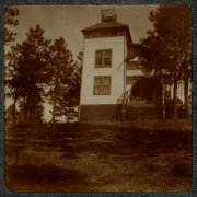 View of a two-story house in Colorado. The house has an arched porch entrance, rooftop balcony, and lattice work near the steps.