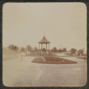 View of gardens and a pavilion in City Park, Denver, Colorado. Sprinklers water the grass and plants.