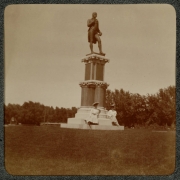 Women in hats and long dresses pose on the base of a statue of Robert Burns in City Park, Denver, Colorado. The base of the statue reads: "Burns".