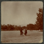 Native American (Ute) women walk in City Park, Denver, Colorado. They wear boot moccasins, dresses, and blankets. Groups of families walk in the distance.