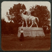 A woman poses near "The Indian," a sculpture by Alexander Phimister (A. P.) Proctor, in City Park, Denver, Colorado. The sculpture depicts a Native American man who holds a spear on horseback.