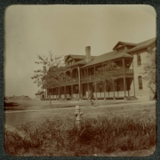 View of a two-story building with a balcony, probably near Denver, Colorado. A man on a bicycle rides between the building and a fire hydrant.