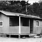 Shows the single story garage and pump house at the Evergreen Golf Course in Dedisse Park 2 miles west of Evergreen, Jefferson County, Colorado. The structure features a small covered porch with a overhang and vertical siding.