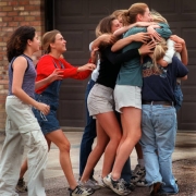 A student just evacuated from the school is embraced by friends overjoyed she is safe.