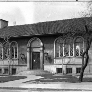 A view of the William N. Byers branch library located on West 7th Avenue and Santa Fe Drive in Denver, Colorado. The one-story building features a stucco exterior, arched windows and doorway, chimneys and red tile roof.