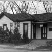 An exterior view of the Eugene Field Library located on East Exposition and South Franklin Street in Denver, Colorado. The single story cottage belonged to Denver poet Eugene Field. The building features wood siding, tiled roof, and a covered porch. A sign that hangs from the porch roof reads: "Eugene Field Library".