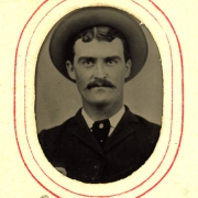 Studio portrait of Cameron. He has a moustache and wears a suit, tie, and wide-brimmed hat.
