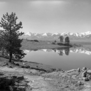 Trees and mountains are reflected in De Weese Reservoir, Custer County, Colorado; wide fields and the Sangre De Cristo Range are in the background.