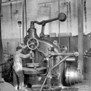 Interior of the Denver Tramway Company machine shop; a worker operates a large drill press.