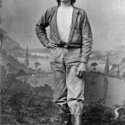 Standing studio portrait of an unidentified miner, Colorado. He wears boots, pants, coat, and hat. He sports a bushy mustache and shoulder length hair.