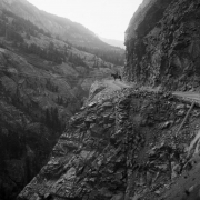 View of the Otto Mears toll road in Uncompahgre Gorge, Ouray County, Colorado; shows a man on a horse, power poles, and cliffs.
