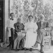Family portrait with grandparents, and a mother and son, probably Doug Ellis, seated on a porch bench, probably in Denver, Colorado.