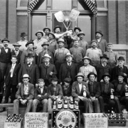 Men and boys pose with cigars, pipes, shovels, a broom, and beer bottles. Crates and labels read: "Tivoli Union Brewing Co. 1342 10th St Denver, Colo."