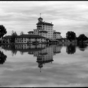 Exterior, back view of the Broadmoor Hotel in Colorado Springs, Colorado; surface of lake reflects hotel image; men and horse-drawn wagon are on opposite shore.