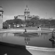 View of the Colorado State Capitol building, Denver, Colorado; shows people standing by the Civic Center reflecting pool and colonnade, trees, and streetcars of the Denver Tramway Company.