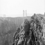 View of Royal Gorge Bridge construction in Fremont County, Colorado; shows steel pylons atop granite cliffs, with cable between.
