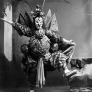 Shows one Chinese actor dressed in full costume. The actor wears a headdress with pheasant feathers, armor and holds two large maces.
