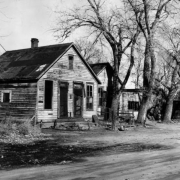 View of abandoned houses on Ninth Street in Denver, Colorado (Lincoln Park Neighborhood); shows dilapidated frame residences and trees.