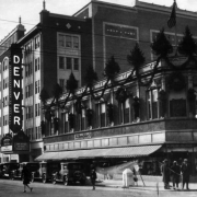 View of the Denver Theater, at 1545 Glenarm Place in Denver, Colorado; shows Glenarm Place, parked automobiles, and "The Powers Behen Co." building at 510 16th (Sixteenth) Street. The marquee reads: "Pride of the Rockies."