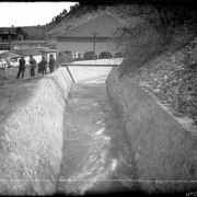 View of the Commmunity Canal at Eldorado Springs (Boulder County)  Colorado; shows a rock walled water channel, men and a team of horses by a footbridge, the swimming pool pavilion, and a hotel and cabins.