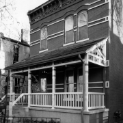View of 2754 Stout Street in the Curtis Park neighborhood (Five Points) in Denver, Colorado; shows a brick house with corbeling and brackets; a man works on the covered porch.