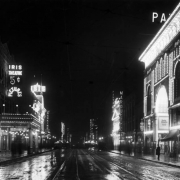 View of Curtis Street, in Denver, Colorado; shows wet pavement, and electric signs: "Iris Theatre 5 cent Pictures," "Isis," "The Nanking Chop Suey," "Princess," "St. James," "Tabor Grand," "Marquette Hotel," "Pantages," and "Paris Theater."