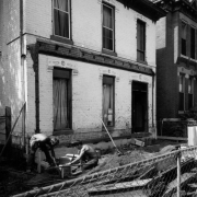 View of 2831 Curtis Street in the Curtis Park neighborhood (Five Points) in Denver, Colorado; shows a brick house with lintels. Men set forms for a new porch foundation.