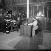 Interior view of Daniels and Fisher store offices in Denver, Colorado; shows a man, a woman, a roll top desk, a telephone, spittoon, and file cabinets.