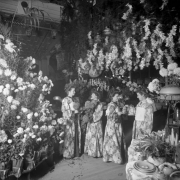 Interior view of the Daniels and Fisher store in Denver, Colorado; shows women in brocade kimonos holding chrysanthemums and pouring tea. Lamps, a plant, and dishes are on a table.