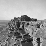 View of Walpi Pueblo, First Mesa, Arizona, shows: adobe and masonry dwellings overlooking a wide valley; stone corrals at the base of the steep rock walls.