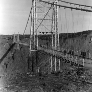 Tourists walk across the Royal Gorge Suspension Bridge, Fremont County, Colorado, over 1000 feet above the Arkansas River. American flags decorate the tall towers for the dedication of the 1260 foot long and 18 feet wide bridge. Built by the Royal Gorge Bridge and Amusement Company in six months, dedicated on December 6, 1929.