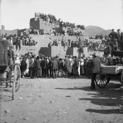 View of Taos Pueblo, New Mexico, during the San Geronimo Day festival; shows a crowd of spectators including Native Americans (Taos Pueblo) and whites. Many sit on adobe pueblo dwellings.
