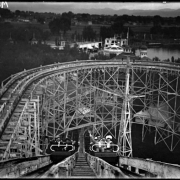 View of riders on a roller-coaster at White City amusement park (later called Lakeside) west of Denver, Colorado; view taken from top of incline looking down at two car-loads of waving riders.