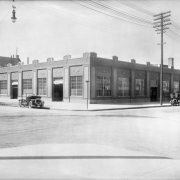 View of a building on the corner of 13th (Thirteenth) Avenue and Lincoln Street in downtown Denver, Colorado. The one-story building has decorative brickwork and garage doors. Cars are parked nearby.