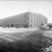View of the Lindquist Cracker and Candy Company building at 3512 Walnut Street in the Five Points neighborhood of Denver, Colorado. Cars and horse-drawn wagons are nearby. A sign on the three-story brick building reads: "The Lindquist Cracker & Candy Co."
