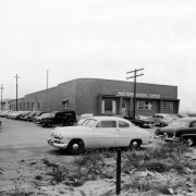 View of Western Bakers Supply, at 4969 Colorado Boulevard, in Denver, Colorado; shows a brick building, and parked cars. A van reads: "Cunningham's Restaurant."