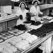 Interior portrait of employees at Mrs. Stover's Candy factory, in Denver, Colorado; women wear caps and pose with cakes and chocolate truffles.