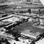 Aerial view of the Denver Rock Drill Manufacturing Company buildings at 40th (Fortieth) Avenue and Williams Street in the Elyria neighborhood of Denver, Colorado. A water tower is among the industrial buildings. Railroad cars and tracks are in the distance.