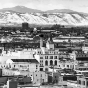 View of Denver, Colorado; shows the Tivoli Brewery in the Auraria neighborhood, surrounding warehouses, and office buildings. Snow dusts front range mountains in the background.