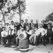 Portrait of Tivoli-Union Brewery employees in Denver, Colorado, posing with beer mugs, kegs, and a pitcher.