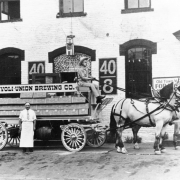 View of a horse drawn wagon in Denver, Colorado; men pose; sign reads: "Tivoli-Union Brewery."